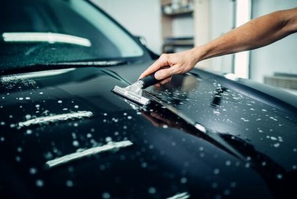 Picture of man's arm applying protective clear bra to hood of a car